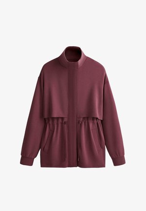Giacca bordeaux con cerniera, collo alto, vita con coulisse elastica, maniche lunghe con polsini, tasche frontali e dettaglio in tessuto a strati sul petto.