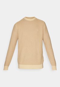Béžový pletený svetr s kulatým výstřihem, dlouhými rukávy a ribbovanými manžetami a lemem. Na přední straně má jemné logo.