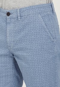 Pantaloni bărbați de culoare albastru deschis cu un model geometric, având închidere cu nasturi și buzunare laterale. Textura materialului este netedă.