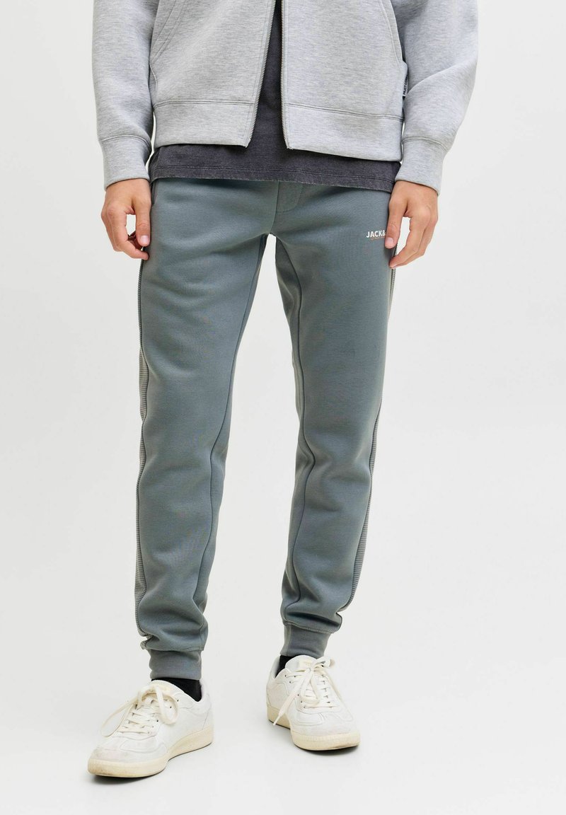Graue Sweatpants aus weichem Material mit schmalem Schnitt, elastischen Bündchen und seitlichen Streifen. Ein kleines Logo befindet sich auf der Vorderseite.