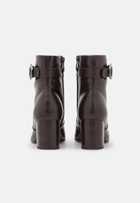 Par de botas de cuero marrón oscuro hasta el tobillo con acabado texturizado, tacones cuadrados, cremalleras laterales y correas decorativas con hebillas metálicas redondas.