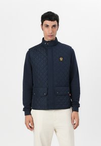 Marineblå quiltet gilet med høy krage, utstyrt med et logo-lapp og to frontlommer; glatt tekstur og knappefeste.