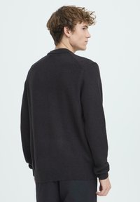 Pulover tricotat închis la culoare, cu decolteu rotund, manșete și tiv striate, și croială lejeră. Textura pare moale și fină.