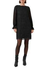 Czarna sukienka z teksturowanej tkaniny o splocie, z długimi przezroczystymi rękawami i okrągłym dekoltem. Posiada prostą sylwetkę i długość za kolano.