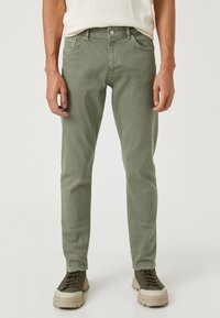 Slim fit, olivgröna bomullbyxor med fem fickor, bälteslingor och en lätt struktur, parat med gråbruna snörskor.