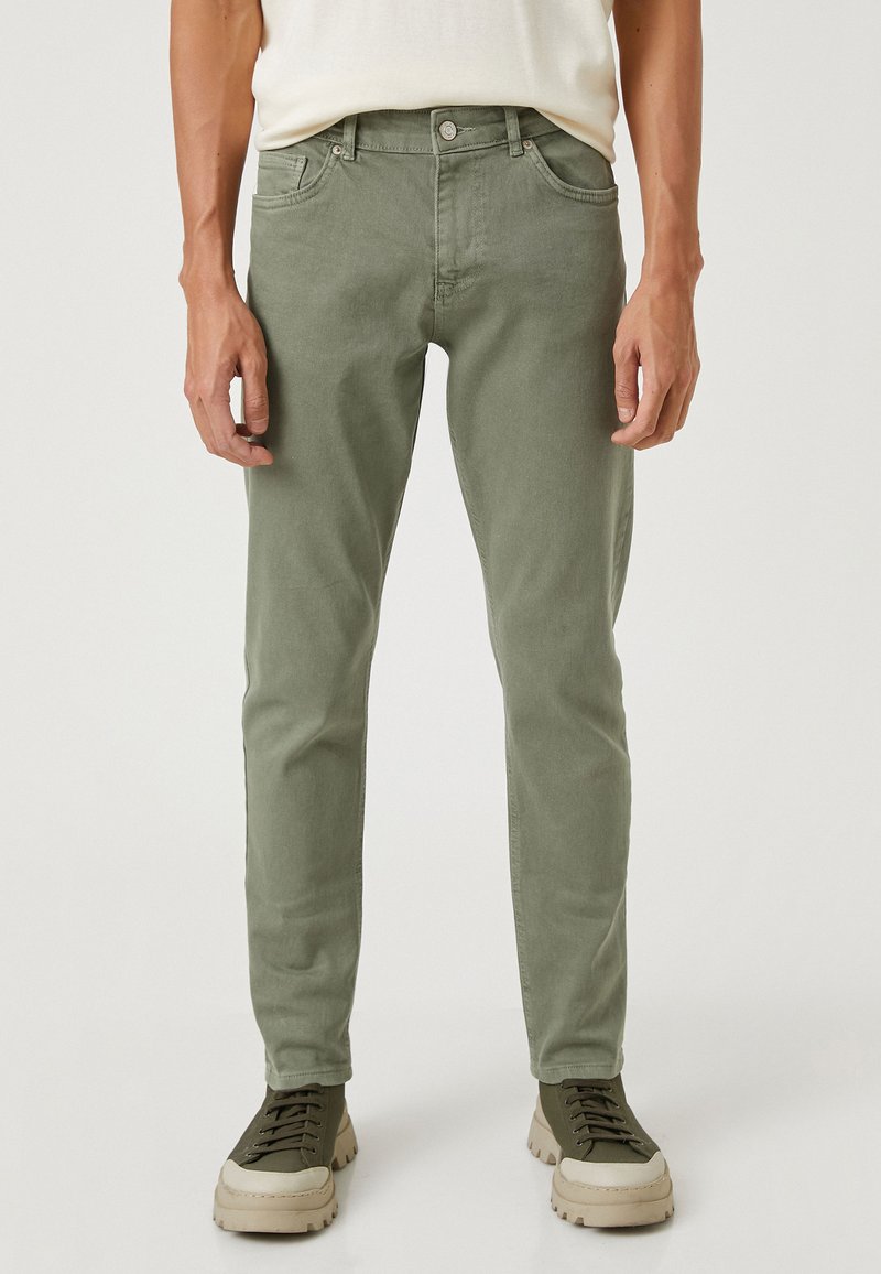 Slim fit, olivgröna bomullbyxor med fem fickor, bälteslingor och en lätt struktur, parat med gråbruna snörskor.