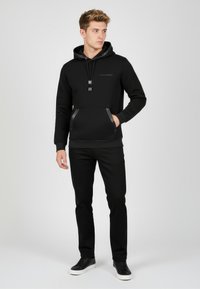 Felpa nera con cappuccio e tasca frontale, con dettagli e coulisse nere. Paio di pantaloni neri e sneakers nere.