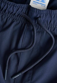 Ceinture élastique bleu marine avec cordon tressé sur un pantalon décontracté, avec une étiquette de marque Jack & Jones à l'intérieur du vêtement.