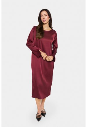 Bordeauxfarbenes Satin-Kleid mit langen Ärmeln und geradem Schnitt, rundem Ausschnitt und glatter Textur, kombiniert mit schwarzen spitzen High Heels.