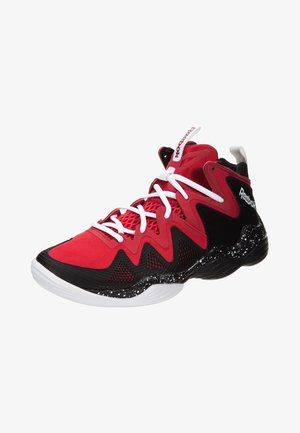 Chaussure de sport rouge et noire avec une tige texturée, un motif en zigzag, des lacets blancs et une semelle intermédiaire noire tachetée. Logo Reebok sur le côté.