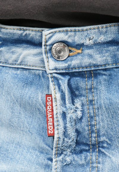 Un jean en denim bleu clair présente un design classique à cinq poches, une fermeture à bouton et un détail déchiré près de la taille. Étiquette rouge "DSQUARED2" visible.