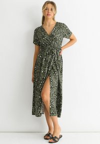 Green leopard print wrap dress with short sleeves, V-neckline, side slit, and tie waist detail. Model wearing black slide sandals.