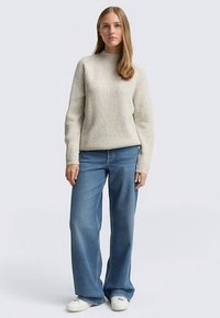 Pulover gri deschis cu guler înalt și mâneci lungi, cu model reiat, asortat cu blugi albaștri cu talie înaltă și croială largă și pantofi sport albi. Design simplu, fără modele.