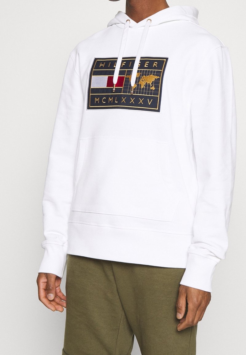 Hvid bomulds-hoodie med en frontlomme, prydet med et farverigt broderet logo-design med et kort og tekst. Elastiske manchetter og kant.