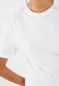 Bílý bavlněný tričko s žebrovaným kulatým výstřihem a krátkými rukávy, s hladkou texturou a uvolněným střihem.