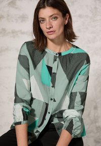 Camicia button-up con motivo geometrico multicolore in teal, nero e bianco; realizzata in tessuto leggero con polsini arricciati.