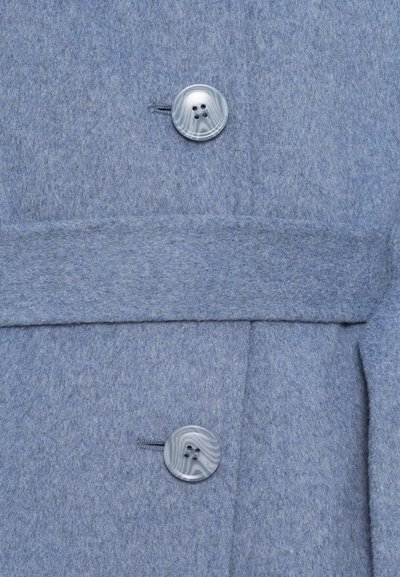 Deux boutons en marbre gris avec un motif, fixés sur un manteau en laine bleu, avec une couture horizontale et un rabat de poche.
