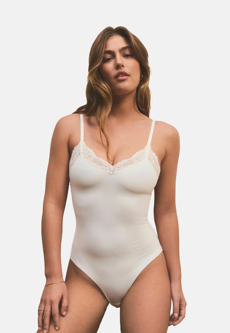 Bodysuit mit Spitzenbesatz in hellem Creme, ausgestattet mit dünnen, verstellbaren Trägern, einem taillierten Schnitt und einer glatten, dehnbaren Stoffstruktur.