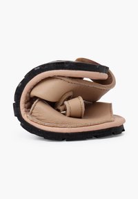Infradito pieghevole con tomaia in pelle beige e suola in gomma nera, caratterizzata da un design arrotondato e da una minimalistica presenza di componenti metallici.