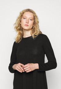 Abito lungo nero con maniche lunghe realizzato in un tessuto morbido e leggero, con scollatura tonda e vestibilità comoda, caratterizzato da una leggera texture e dettagli delle cuciture.