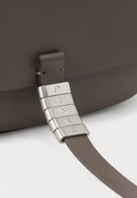Cinghia della borsa a spalla in pelle marrone con hardware argentato che presenta lettere incise che formano la parola "PINKO", mostrando una texture liscia e un design piatto.