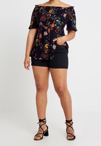 Top floral sin mangas en un oscuro azul marino con mangas acampanadas, combinado con pantalones cortos negros y sandalias de tacón cuadrado negro con tiras.