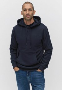 Mörkblå hoodie i mjukt tyg, med en framficka, dragsko huva och ribbade muddner. Kombinerad med ljusblå jeans.