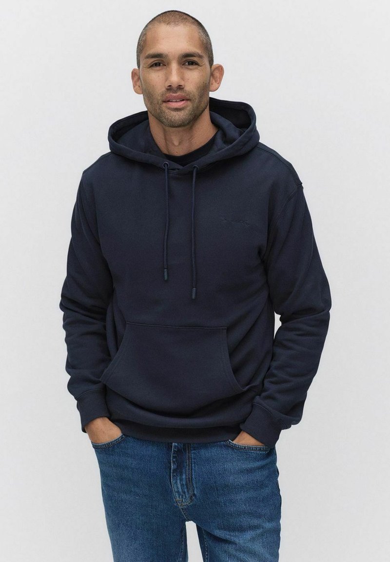 Mörkblå hoodie i mjukt tyg, med en framficka, dragsko huva och ribbade muddner. Kombinerad med ljusblå jeans.