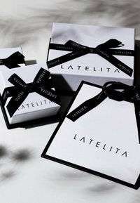 Vita gåvor i vitt med svarta accenter, med "LATELITA"-märkning och svarta band. Inkluderar små och stora storlekar. Slät yta.