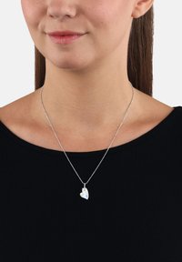 Collana in argento con pendente a forma di cuore caratterizzato da una superficie sfaccettata e iridescente, indossata su una maglia nera a coste.