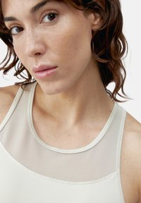 Lys beige trenings tank topp med mesh-overlegg ved utringningen, med flate sømmer og en jevn tekstur.