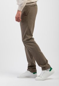 Pantaloni khaki slim fit, con frontale piatto, tasche laterali e una tasca posteriore con bordino nero, abbinati a sneakers bianche.