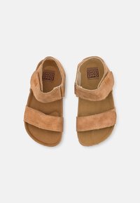 Sandalias de cuero marrón con dos correas de velcro ajustables, plantilla texturizada y una suela redondeada y lisa. Logotipo visible en las plantillas.
