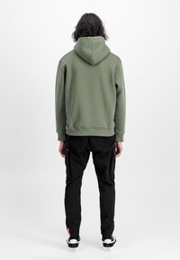 Olivgrüner Hoodie mit Kapuze, ausgestattet mit gerippten Bündchen und Saum. Kombiniert mit schwarzen Cargo-Hosen und weißen Sneakers. Einfaches, lässiges Design.