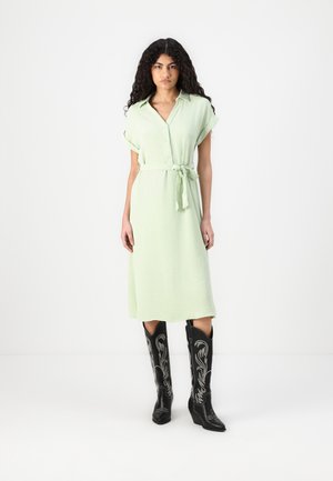 Light green shirt dress with a belt, short rolled sleeves, and a button-down front. Black cowboy boots with silver embroidery.