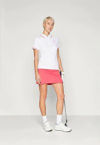 Λευκό πόλο μπλουζάκι με κόκκινες λεπτομέρειες συνδυασμένο με ροζ φούστα. Το σύνολο είναι φτιαγμένο από ελαφρύ ύφασμα, κατάλληλο για αθλητική ένδυση.