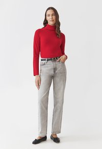 Pulover roșu cu gât înalt, blugi gri deschis cu talie înaltă, curea neagră și pantofi slip-on negri. Textură netedă, design simplu.