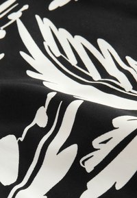 Čierna látka s veľkým bielym kvetinovým vzorom, zobrazujúca výrazné listy a abstraktné tvary v detailnom zábery.