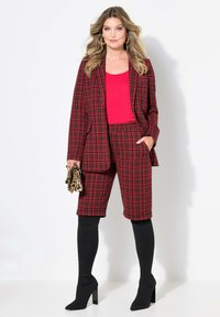 Röd och svart rutigt blazer med matchande shorts, kombinerat med en röd linne och svarta knähöga stövlar. Accessoarer med en guldfärgad clutch.
