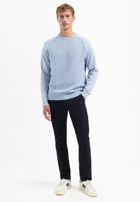 Lichtblauwe textuurtrui met ronde hals en raglanmouwen, gecombineerd met donkere broeken en witte sneakers met marineaccenten.