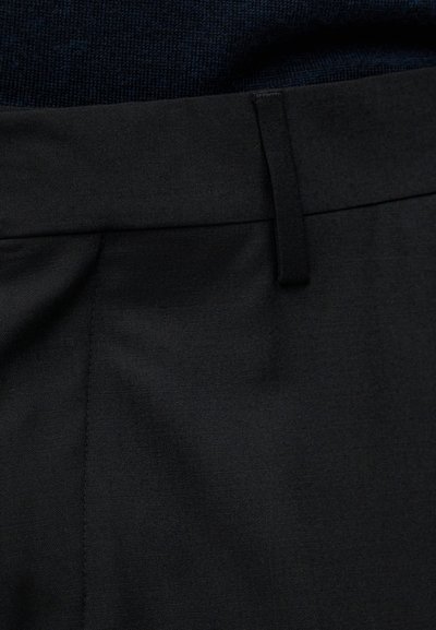 Close-up van de tailleband van een zwarte broek met broeklus en donker getextureerde stof zichtbaar boven de tailleband.