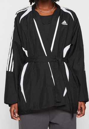 Sort letvægtsjakke med en indpakningsdesign, hvide diagonale striber og lange ærmer. Har et bælte i taljen og en tekstureret overflade.