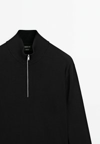 Zwarte sweater met ritssluiting, gemaakt van katoen. Beschikt over een hoge kraag, geribbelde brei-textuur en een minimalistisch ontwerp zonder patronen.