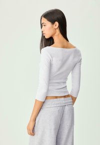 Gray long-sleeve top with a wide neckline, fitted design, and soft texture; paired with light gray sweatpants featuring an elastic waistband.
