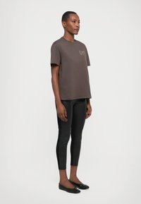 Brown cotton t-shirt featuring a logo detail on the chest, paired with black fitted leggings and simple black flats.