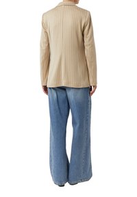 Beige Nadelstreifen-Blazer mit schmaler Passform, kombiniert mit weit geschnittenen blauen Jeans. Der Blazer verfügt über einen Reverskragen und lange Ärmel.