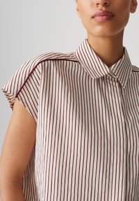 Blusa a righe bianca e bordeaux, con colletto, maniche corte con risvolti e un tessuto leggero e testurizzato.