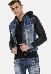 Denim and leather jacket featuring a blue denim body, black leather sleeves, zip closure, and two chest pockets. Textured design with contrasting materials.