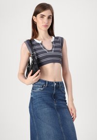 Top scurt cu dungi gri și albe, cu o textură moale și decolteu în formă de V, asortat cu o fustă din denim albastră cu talie înaltă. Modelul ține o geantă neagră.