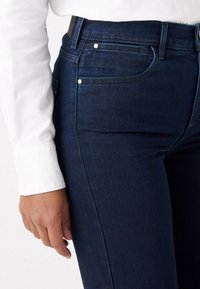 Donkerblauwe denim jeans met vijf zakken, zilverkleurige hardware en een rechte snit, gecombineerd met een witte langlijf top.
